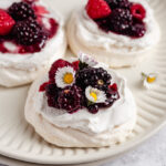 Mini pavlovas topped with berries on a plate