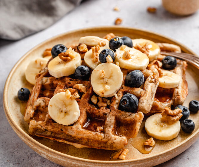 Banana bread waffles on plate with fruit, walnuts, and maple syrup