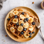 Headshot of waffles topped with bananas, blueberries, walnuts, and maple syrup