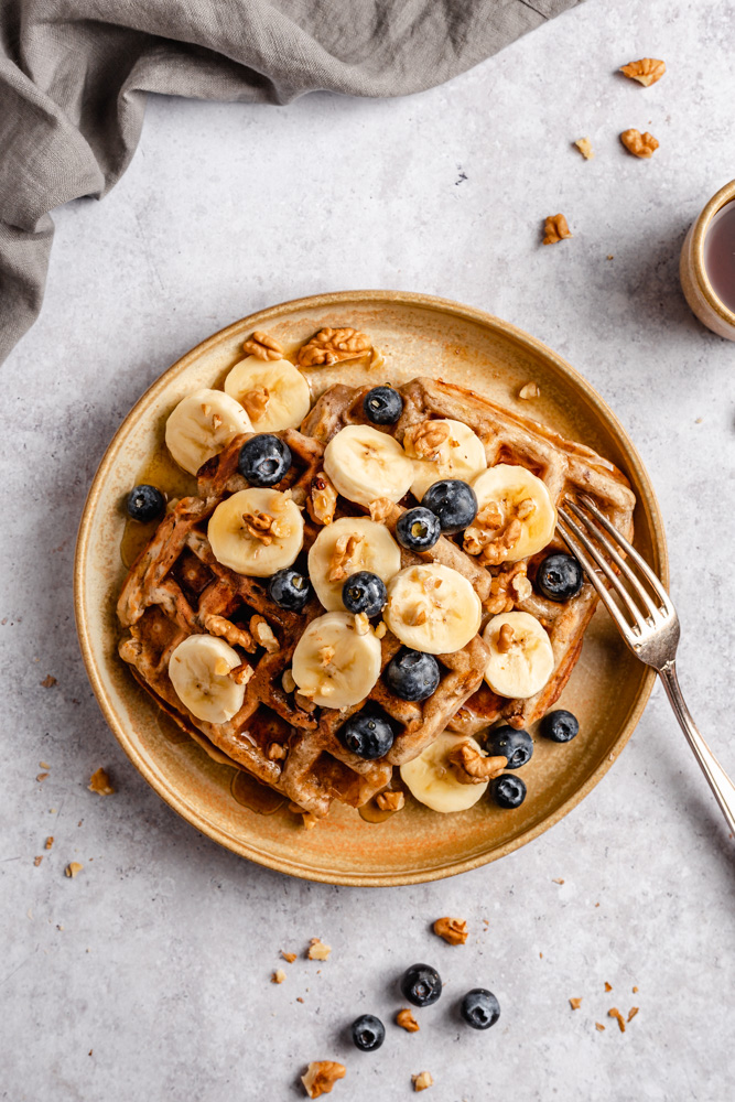Headshot of waffles topped with bananas, blueberries, walnuts, and maple syrup